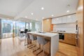 Modern open-plan kitchen with a white island, wooden cabinets, and floor-to-ceiling city views.