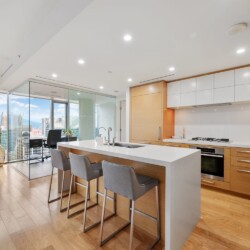 Modern open-plan kitchen with a white island, wooden cabinets, and floor-to-ceiling city views.