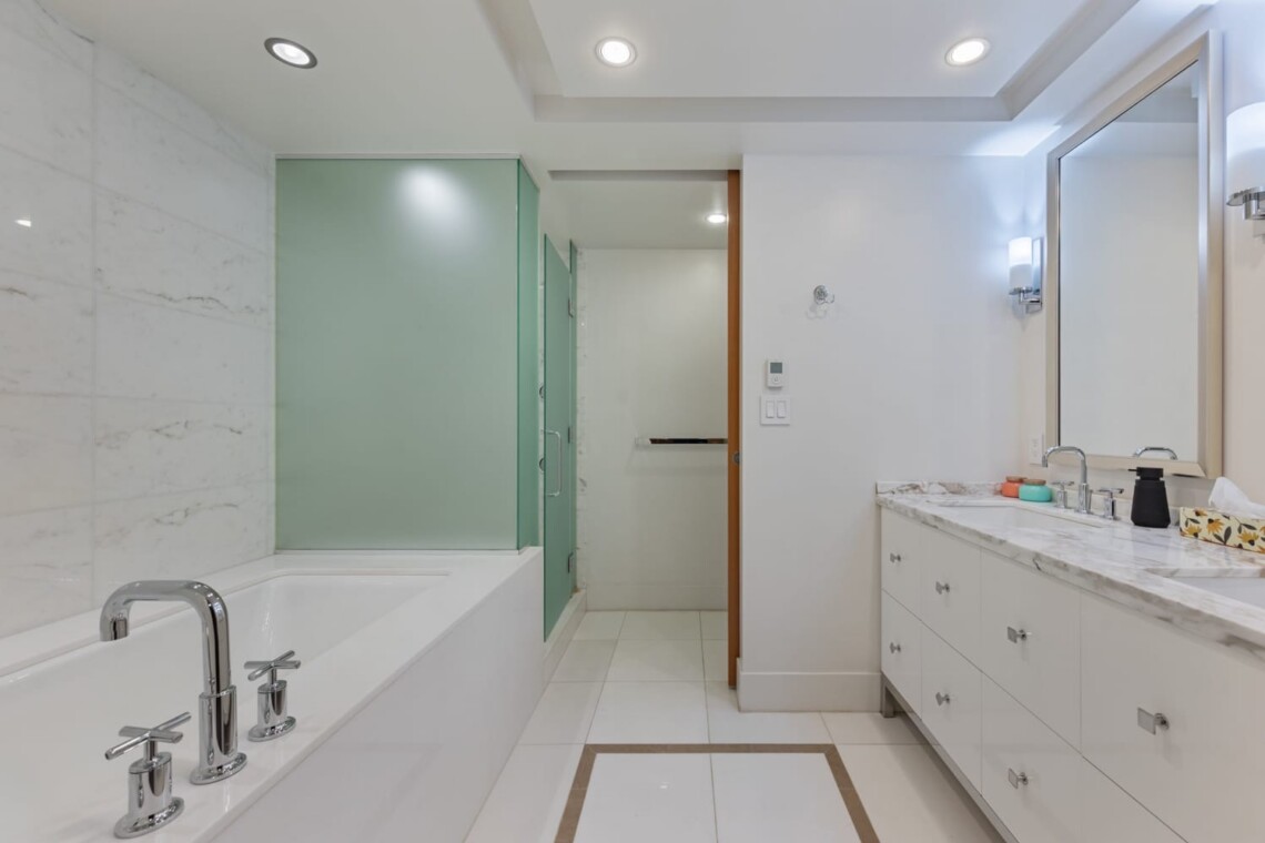 Contemporary bathroom with white marble walls, a built-in tub with chrome faucets, and a frosted green glass shower enclosure.