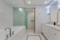 Contemporary bathroom with white marble walls, a built-in tub with chrome faucets, and a frosted green glass shower enclosure.