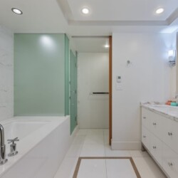 Contemporary bathroom with white marble walls, a built-in tub with chrome faucets, and a frosted green glass shower enclosure.