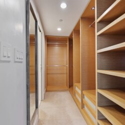 Narrow walk-in closet with built-in wooden shelves and hanging rods, illuminated by ceiling lights