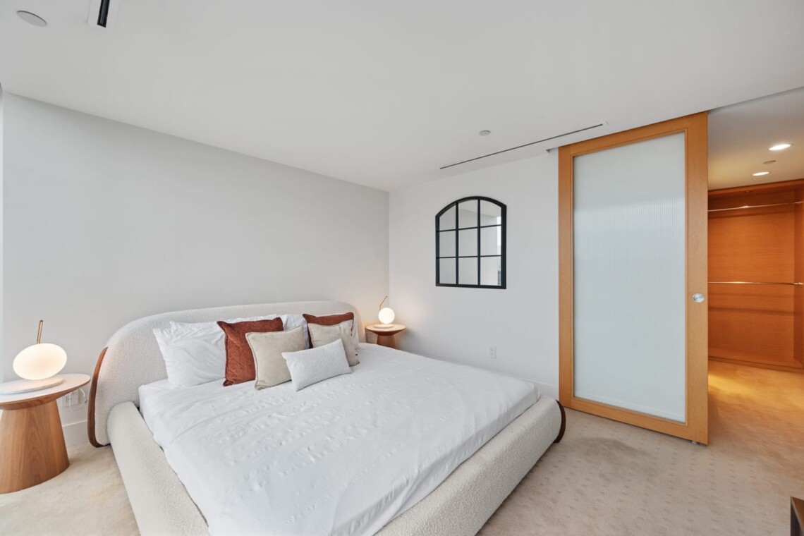 Modern bedroom with a low, plush white bed and assorted throw pillows, two round wooden nightstands with glowing globe lamps.