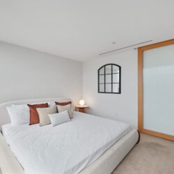 Modern bedroom with a low, plush white bed and assorted throw pillows, two round wooden nightstands with glowing globe lamps.