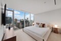 Bedroom with a plush white bed facing floor-to-ceiling windows overlooking a city skyline.
