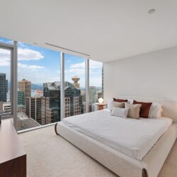 Bedroom with a plush white bed facing floor-to-ceiling windows overlooking a city skyline.