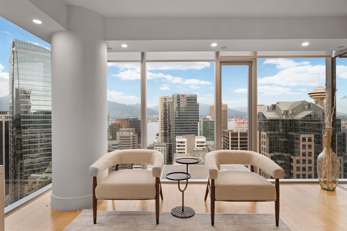 Modern high-rise living area with two beige curved chairs facing large windows that reveal a city skyline and harbor view.
