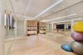 Well-lit boutique fitness studio with wooden floors, wall mirrors, and stacked exercise balls on the right.