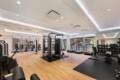 Bright modern gym with wooden flooring, cardio machines by the windows, and a central multi-station strength trainer.