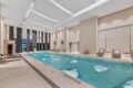Indoor hotel pool area with lounge chairs along the water and tall dark stone columns under a bright ceiling.