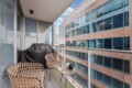 Balcony with wicker chairs and a small glass table overlooking a tall office building with glass windows.