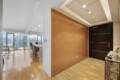 Modern apartment entry with a dark wood door, warm wood accent wall, and city skyline visible through large windows.