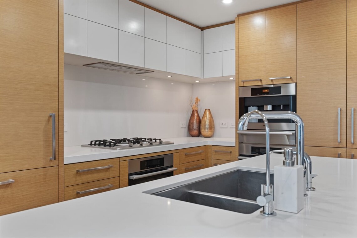 Contemporary kitchen with white countertops and an island sink, surrounded by wooden cabinets and built-in appliances.