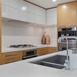Contemporary kitchen with white countertops and an island sink, surrounded by wooden cabinets and built-in appliances.