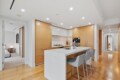Open-plan kitchen with a white island, wooden cabinets, and stainless appliances; bar seating along island with gray stools.