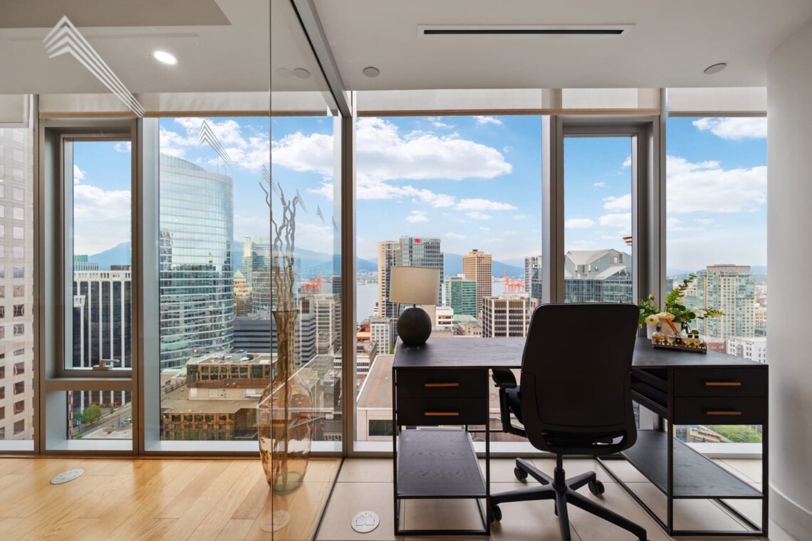 Corner office with a dark desk and chair, overlooking a city skyline through floor-to-ceiling windows.