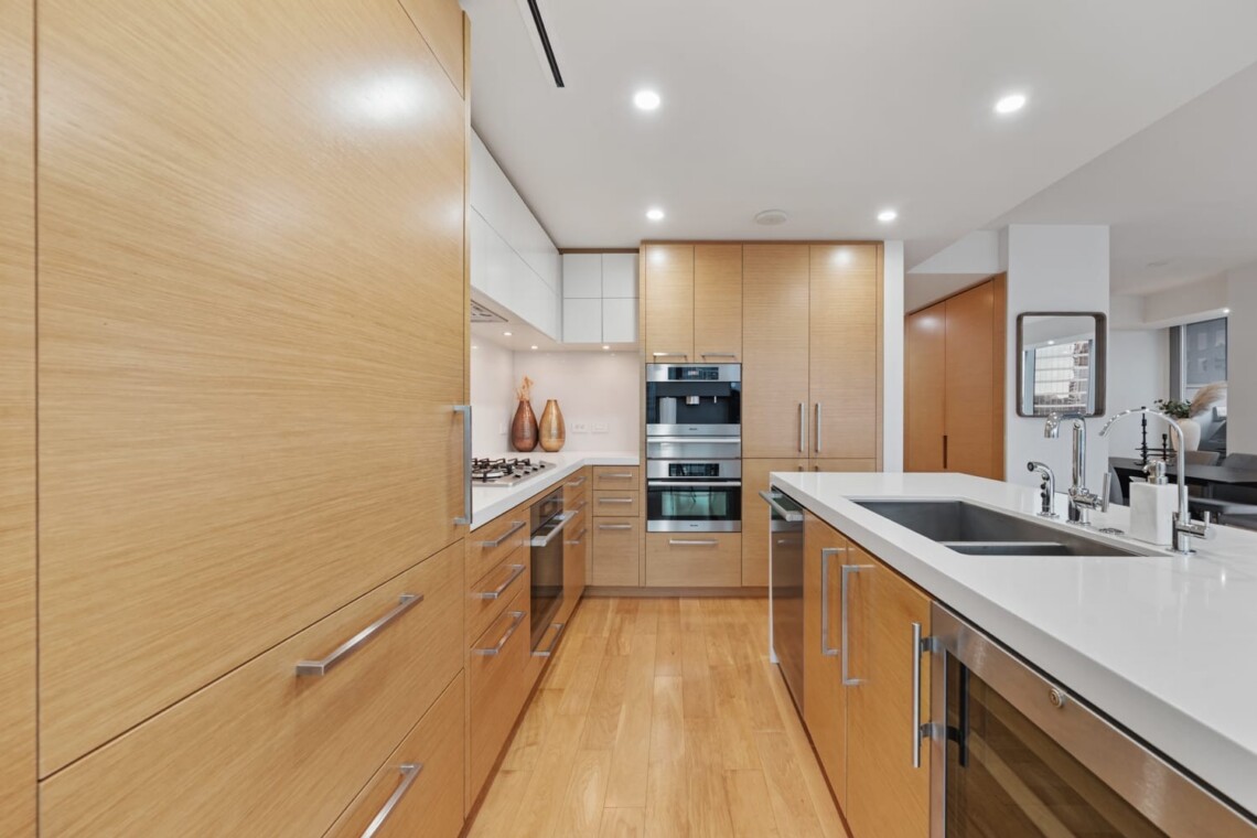 Modern kitchen with light wood cabinets, white countertops, and stainless-steel appliances around a center island with a double sink.