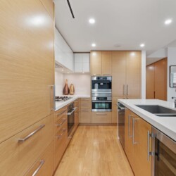Modern kitchen with light wood cabinets, white countertops, and stainless-steel appliances around a center island with a double sink.
