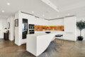 White modern kitchen with a curved island, orange under-cabinet lighting, and built-in ovens in a tall cabinet.