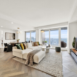 Bright, modern living room with a beige sectional, colorful throw pillows, and large windows overlooking the city skyline.