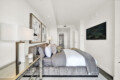 Modern hotel-style bedroom with a gray upholstered bed, abstract art on the wall, and a wall-mounted TV on the right.