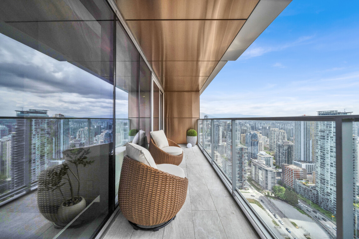 Rattan patio chairs on a glass-walled balcony overlooking a city skyline.