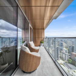 Rattan patio chairs on a glass-walled balcony overlooking a city skyline.