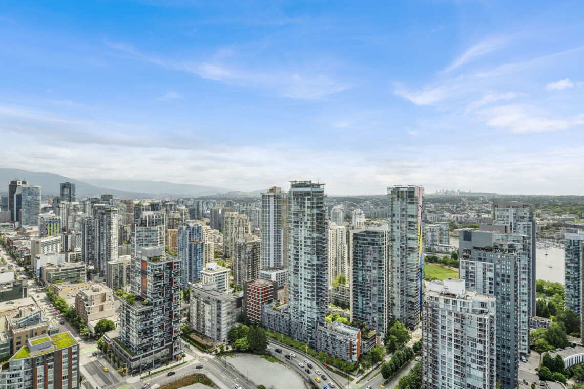 Dense urban skyline with numerous glass high-rise buildings under a clear blue sky, seen from above.