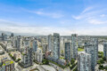 Dense urban skyline with numerous glass high-rise buildings under a clear blue sky, seen from above.