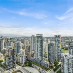 Dense urban skyline with numerous glass high-rise buildings under a clear blue sky, seen from above.