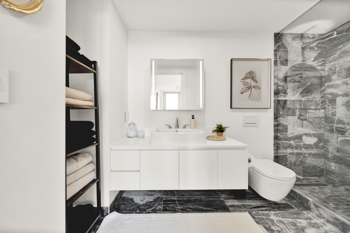 Bright modern bathroom with a white vanity, framed botanical print, and marble-tiled shower area on the right.