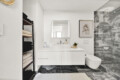 Bright modern bathroom with a white vanity, framed botanical print, and marble-tiled shower area on the right.