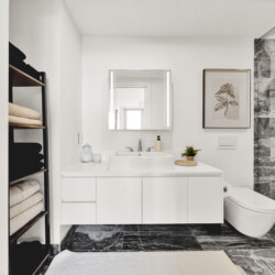 Bright modern bathroom with a white vanity, framed botanical print, and marble-tiled shower area on the right.