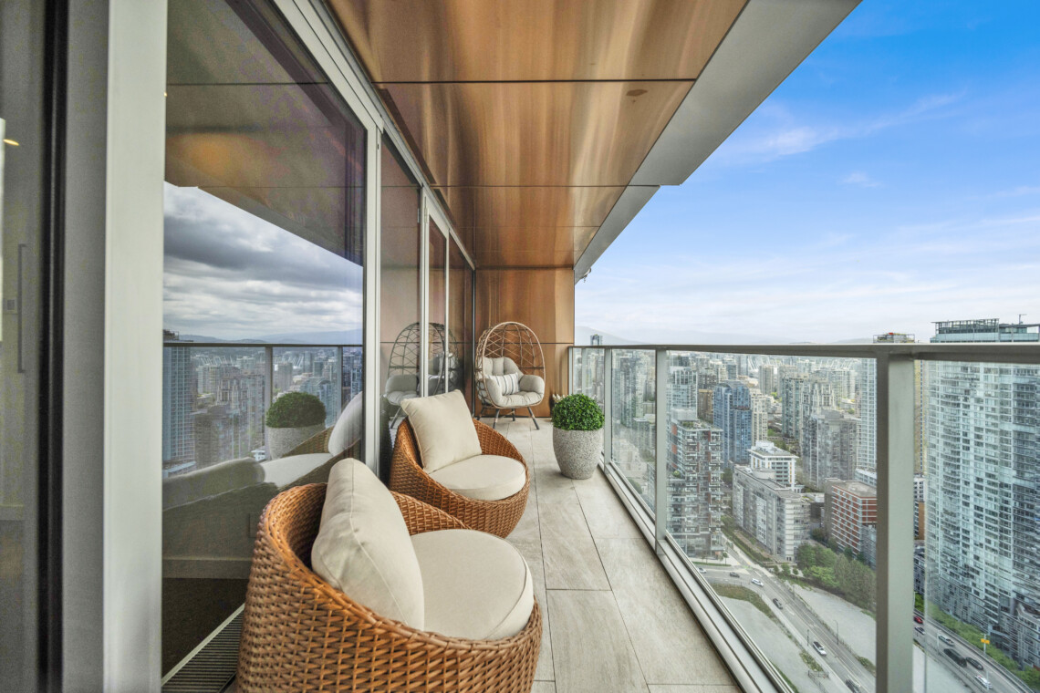 Modern balcony seating with wicker chairs and cushions overlooking a city skyline and blue sky.