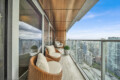 Modern balcony seating with wicker chairs and cushions overlooking a city skyline and blue sky.