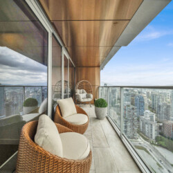 Modern balcony seating with wicker chairs and cushions overlooking a city skyline and blue sky.