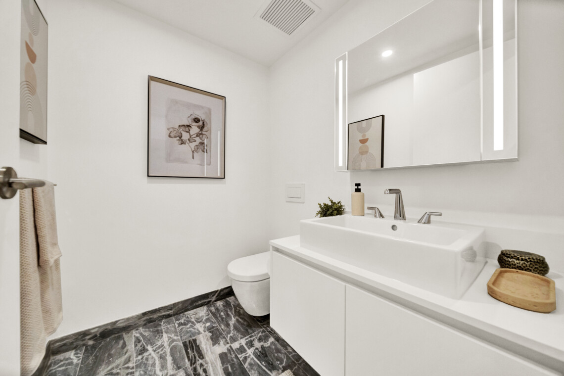 Bright modern bathroom with white vanity, double faucet, and large wall mirror showing framed artwork and soft lighting