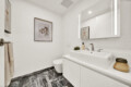 Bright modern bathroom with white vanity, double faucet, and large wall mirror showing framed artwork and soft lighting
