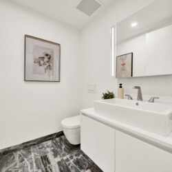 Bright modern bathroom with white vanity, double faucet, and large wall mirror showing framed artwork and soft lighting
