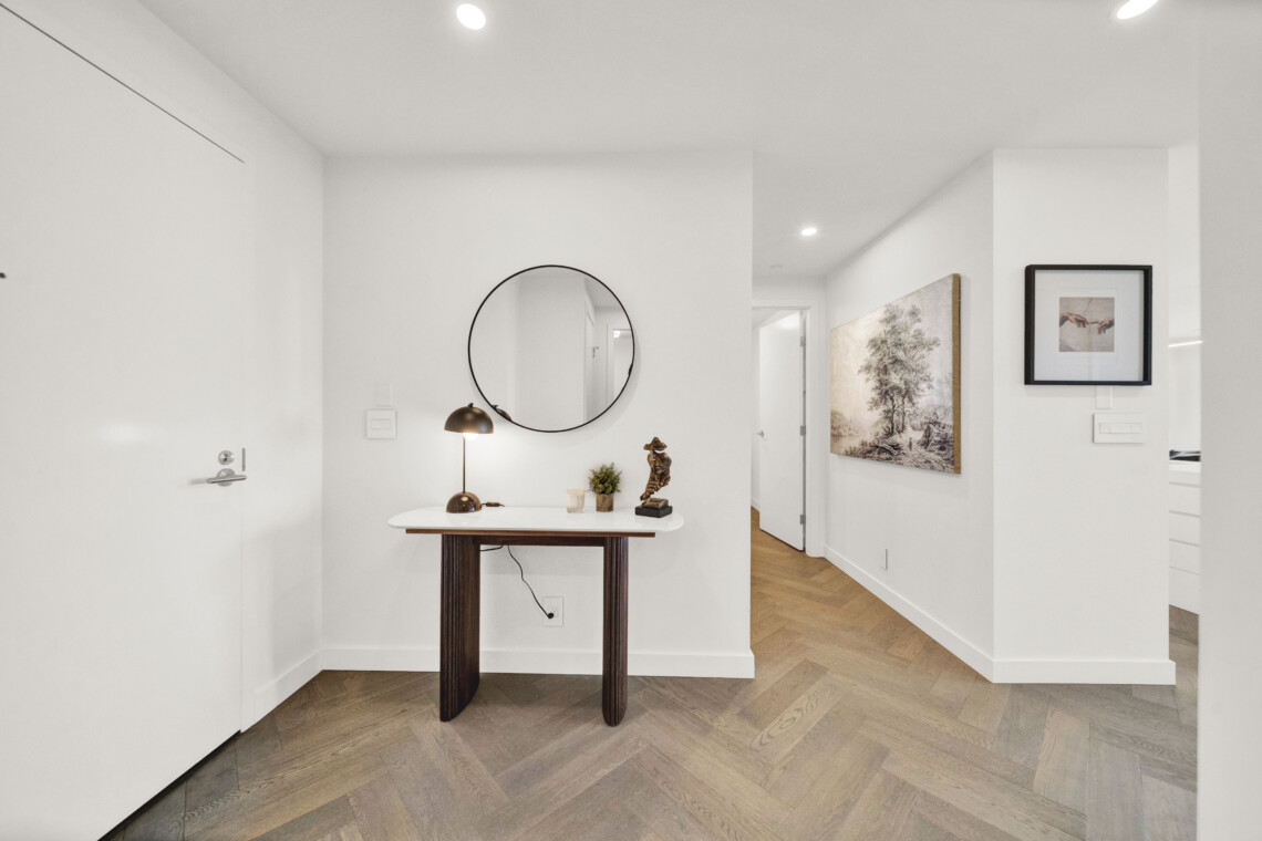 Entryway with white walls, a round wall mirror above a wooden console table, a brass lamp, and small decor pieces.
