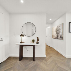Entryway with white walls, a round wall mirror above a wooden console table, a brass lamp, and small decor pieces.