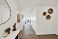 Bright hallway with chevron wood floor, copper wall bowls on the right, a round mirror on the left, and a console table with candles; leads to a living room with a view.