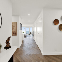 Bright hallway with chevron wood floor, copper wall bowls on the right, a round mirror on the left, and a console table with candles; leads to a living room with a view.