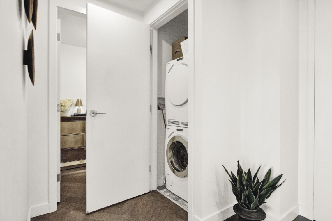 Hallway view into a laundry nook with stacked washing machines and a potted plant in the foreground.