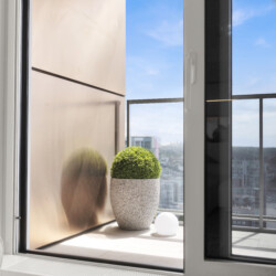 Interior window scene with a round topiary in a speckled gray pot on a sill; blue sky visible outside, white orb nearby.