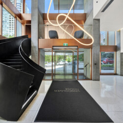 Modern lobby with a large black curved staircase on the left, copper panels, glass doors, and a looping neon sculpture overhead.