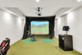 Indoor golf simulator bay with a projection screen, hitting mats, and golf bags along the left wall