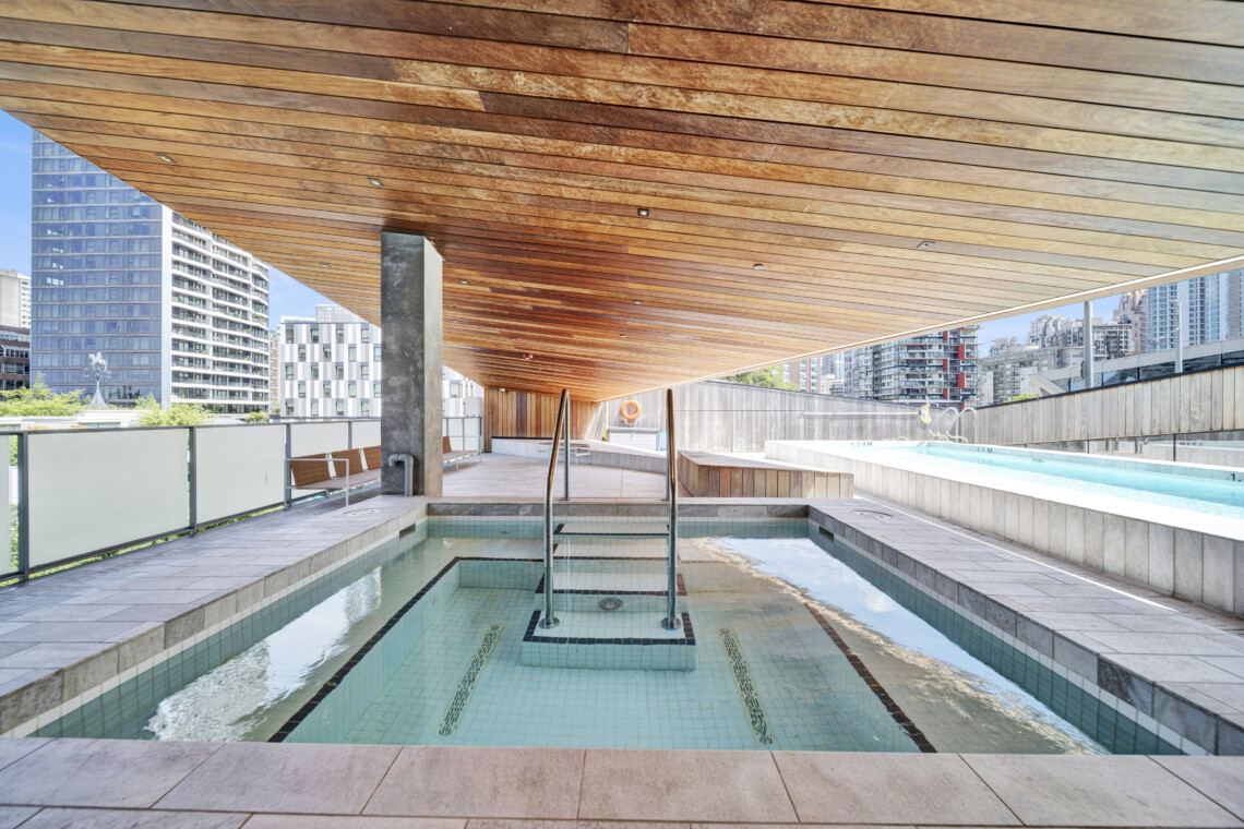 Rooftop pool with turquoise water, wooden slatted ceiling, and city skyscrapers in the background