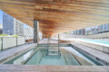 Rooftop pool with turquoise water, wooden slatted ceiling, and city skyscrapers in the background