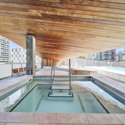 Rooftop pool with turquoise water, wooden slatted ceiling, and city skyscrapers in the background